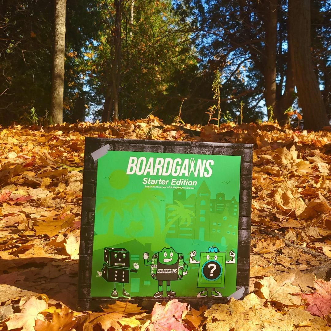 BoardGains Starter Edition game box placed outdoors on a bed of vibrant autumn leaves, with trees in the background. The bright green box stands out against the warm, golden colors of fall, blending nature and fitness in a playful, inviting way.